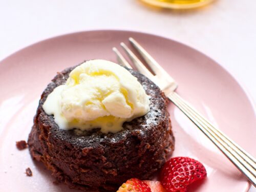 A decadent chocolate lava cake on a plate, served with fresh strawberries and topped with a scoop of vanilla ice cream, creating a delicious dessert presentation.