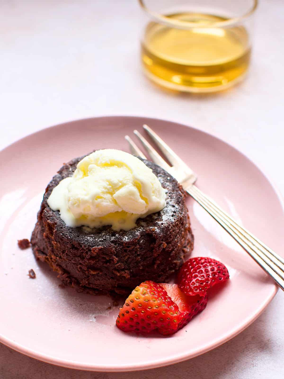 A decadent chocolate lava cake on a plate, served with fresh strawberries and topped with a scoop of vanilla ice cream, creating a delicious dessert presentation.