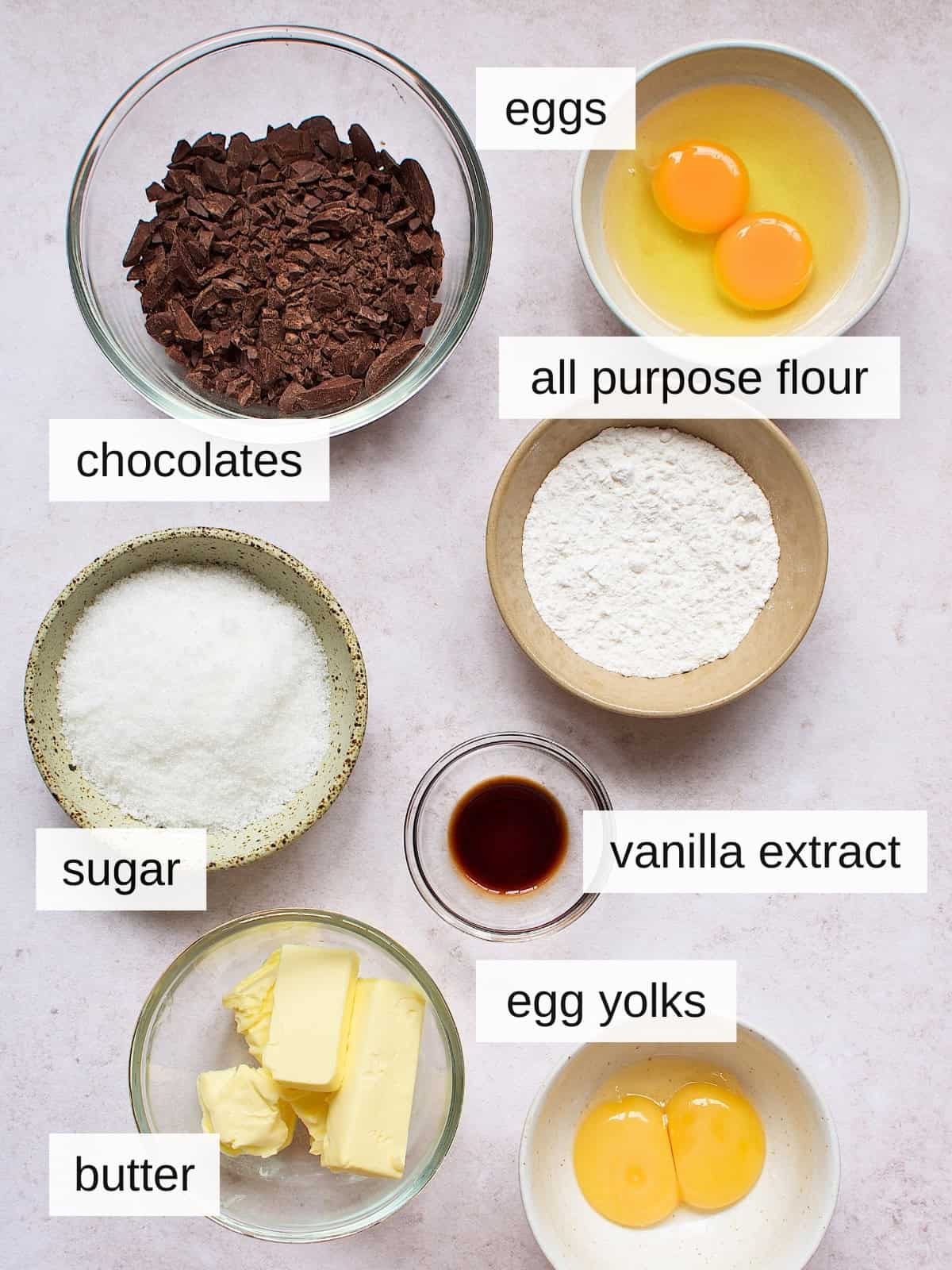 Ingredients for chocolate lava cakes, including eggs, chocolates, all-purpose flour, vanilla extract, sugar, butter, and egg yolks.