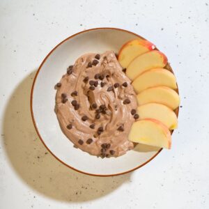 Delicious brownie batter dip topped with chocolate chips, accompanied by sliced apples for dipping.