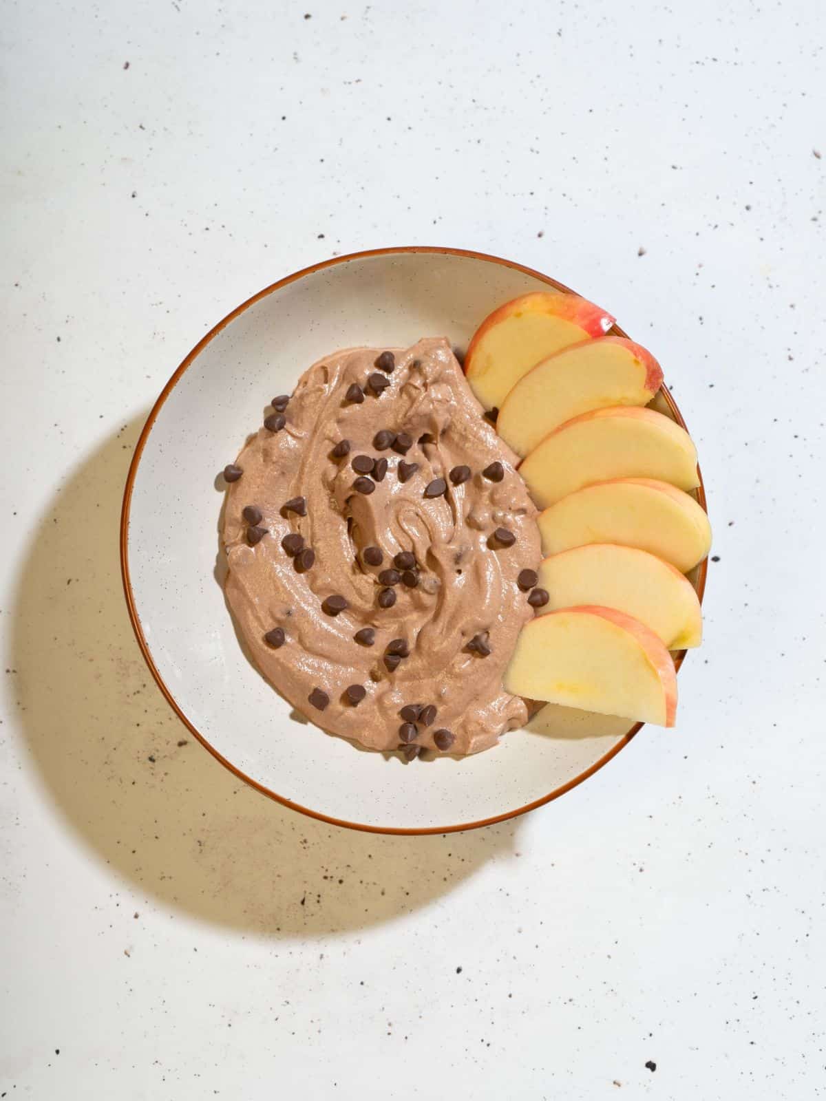 Delicious brownie batter dip topped with chocolate chips, accompanied by sliced apples for dipping.