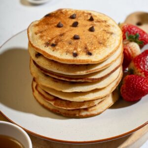 A stack of chocolate chip pancakes served with juicy strawberries, perfect for breakfast.