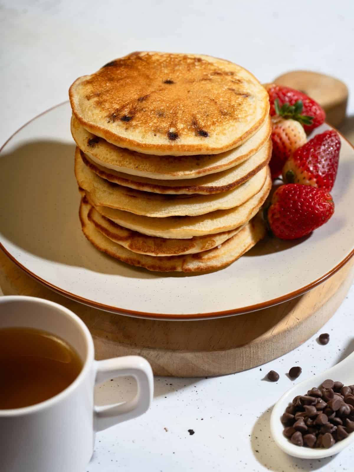 A serving of chocolate chip pancakes stacked and accompanied by fresh strawberries.