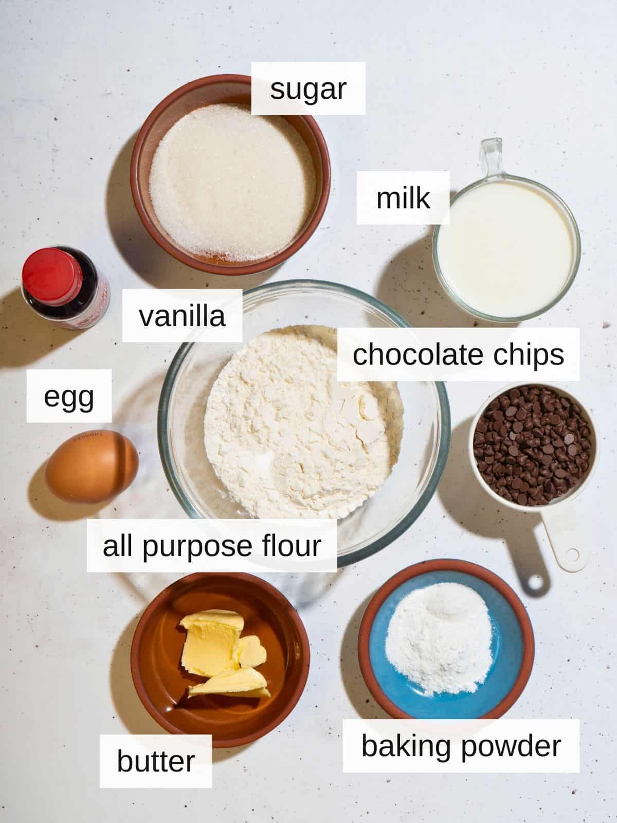 Ingredients for chocolate chip pancakes, including sugar, milk, vanilla, egg, chocolate chips, all purpose flour, butter, and baking powder.
