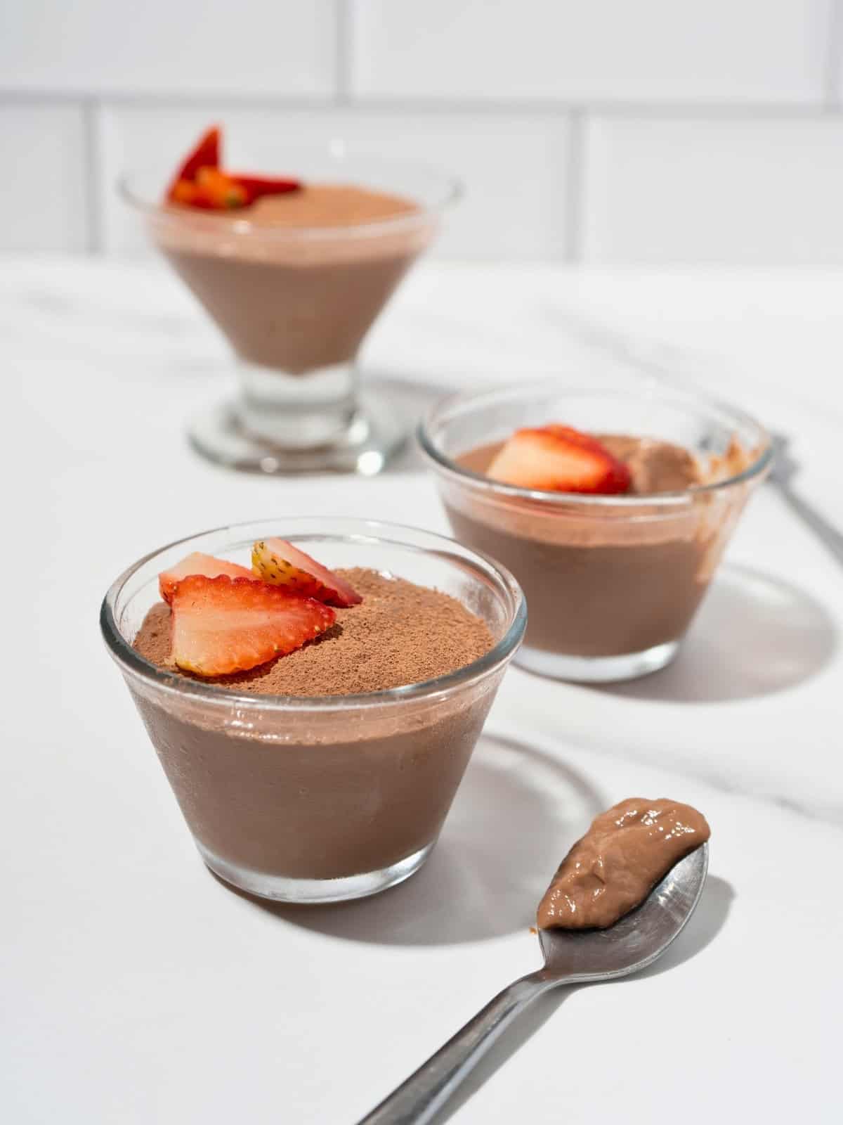 Three glass mugs filled with rich chocolate pudding, each topped with fresh sliced strawberries for a delightful presentation.