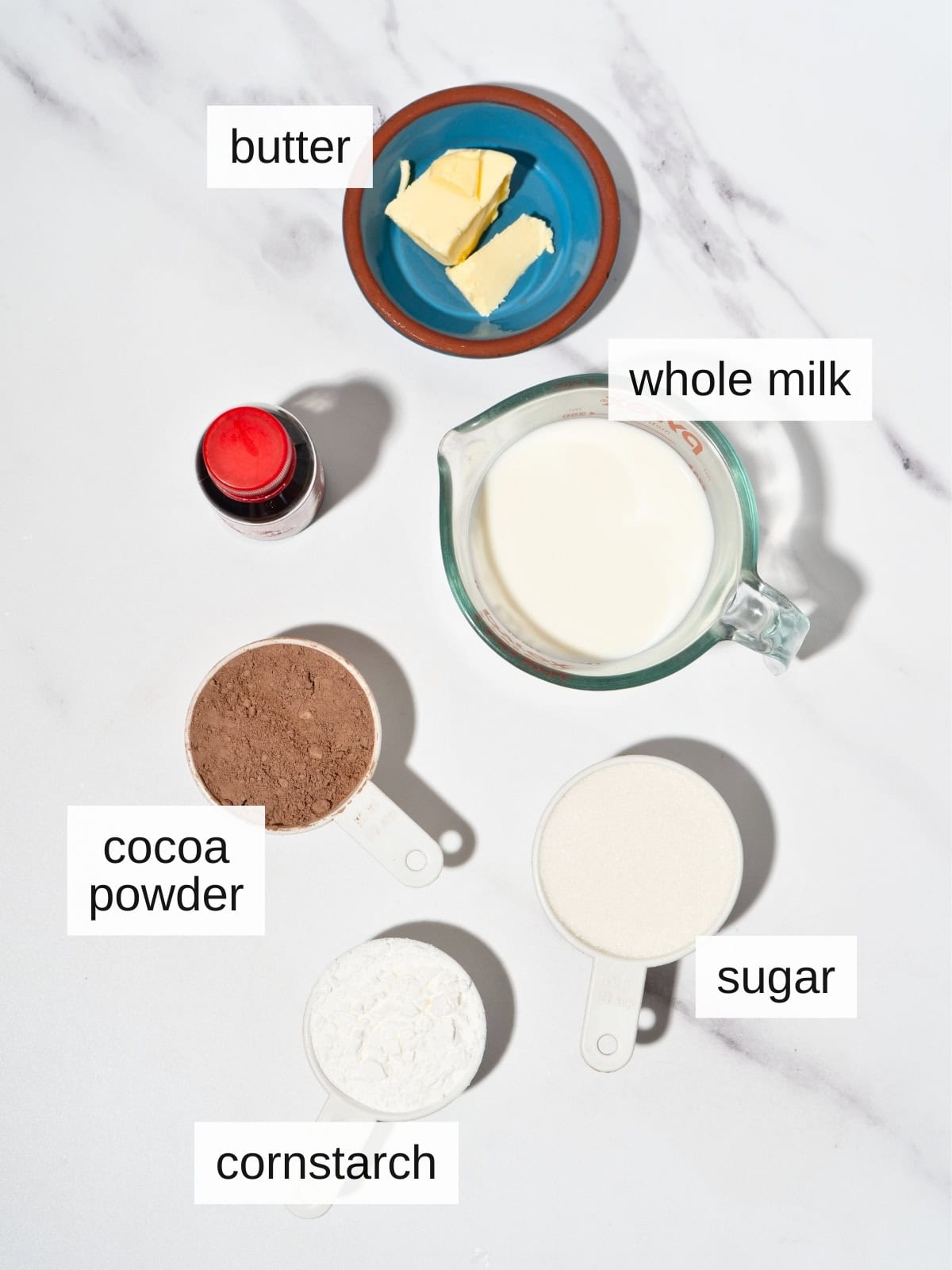 Ingredients for chocolate pudding, including butter, whole milk, cocoa powder, vanilla extract, sugar, and cornstarch.