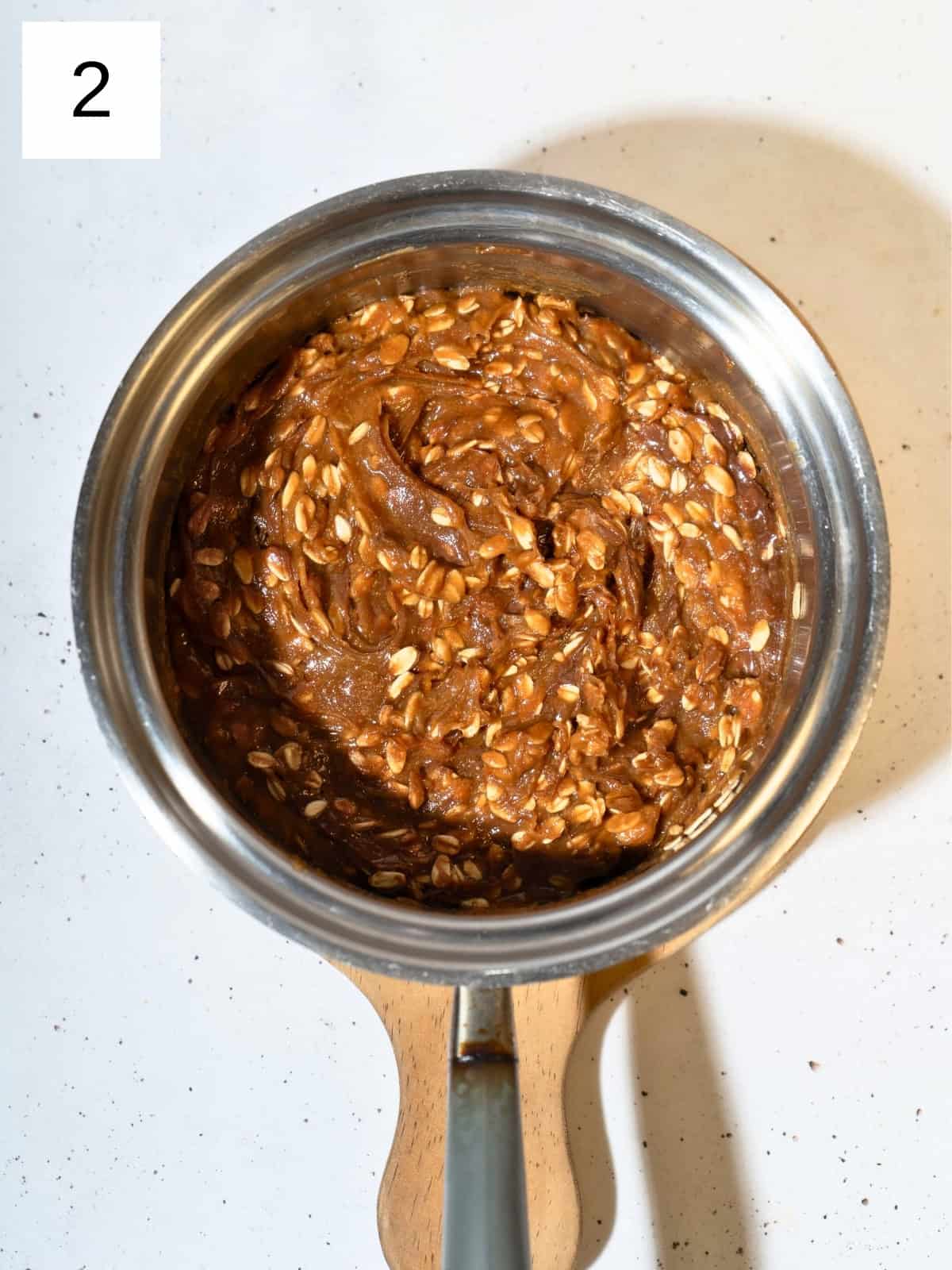 A mixture of peanut butter, maple syrup, salt, vanilla extract, and rolled oats in a a saucepan.