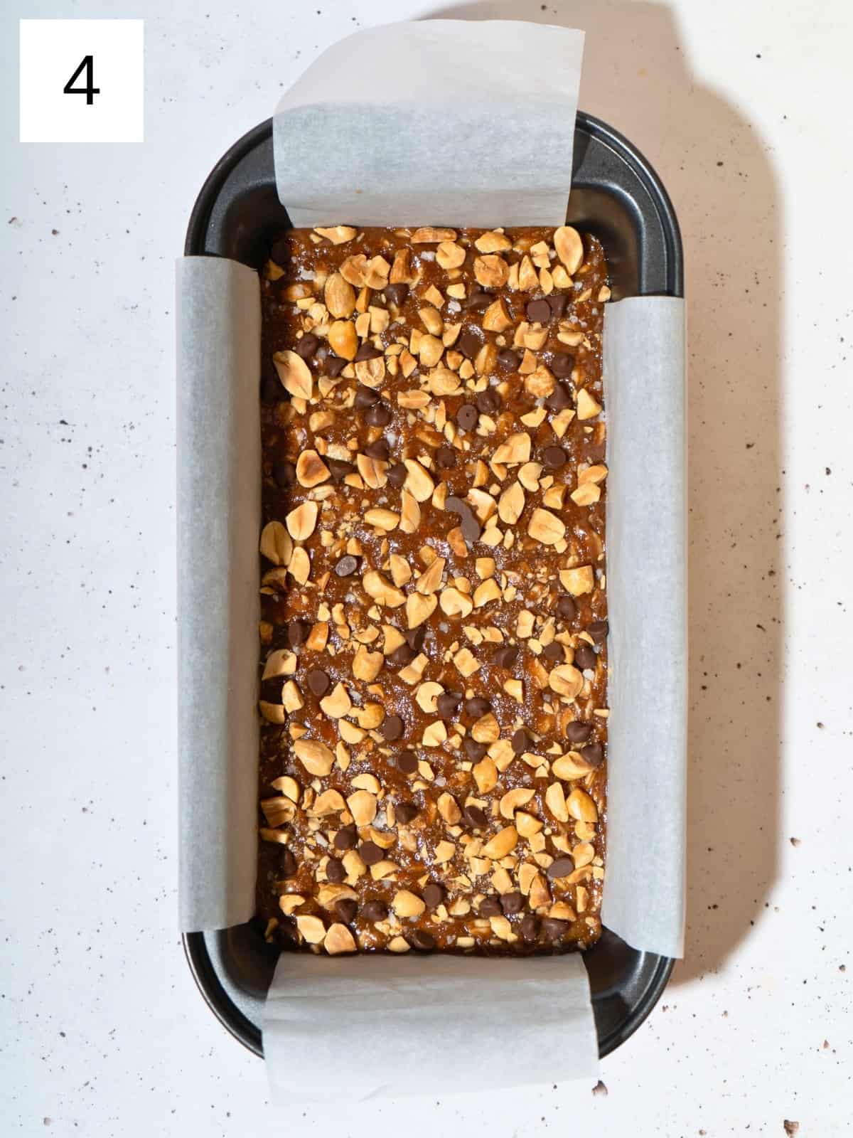 Peanut butter mixture spread in a parchment-lined loaf pan, topped with chopped peanuts and chocolate chips.