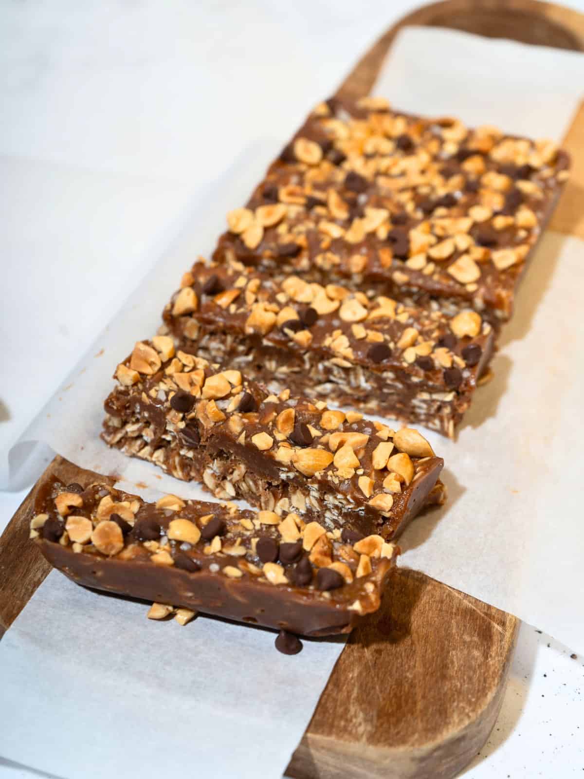 Delicious slices of no-bake peanut butter bars arranged on parchment paper atop a wooden chopping board, showcasing a rich, creamy texture and topped with chocolate chips and chopped peanuts.