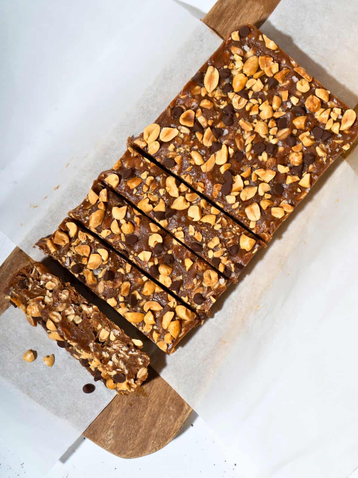 Delicious slices of no-bake peanut butter bars arranged on parchment paper atop a wooden chopping board, showcasing a rich, creamy texture and topped with chocolate chips and chopped peanuts.