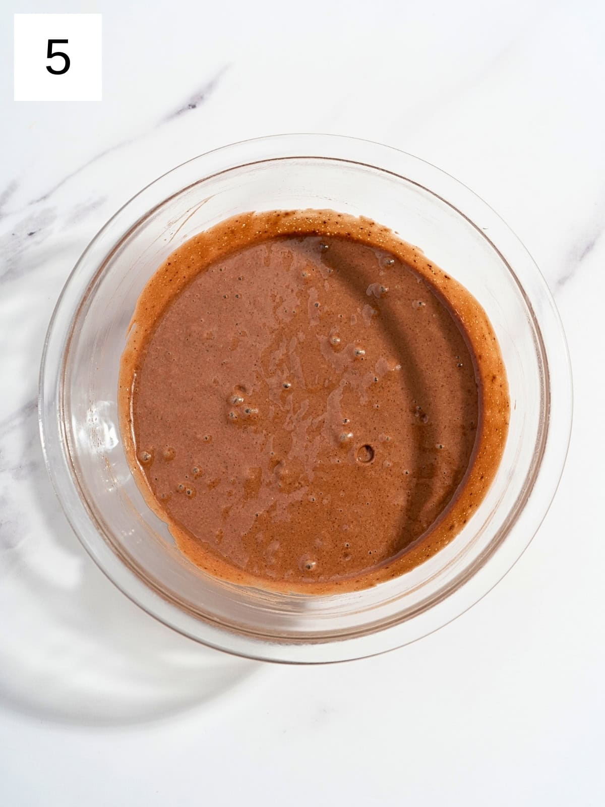 A mixture of dry chocolate mixture ingredients and egg mixture ingredients with boiled water in a glass bowl.