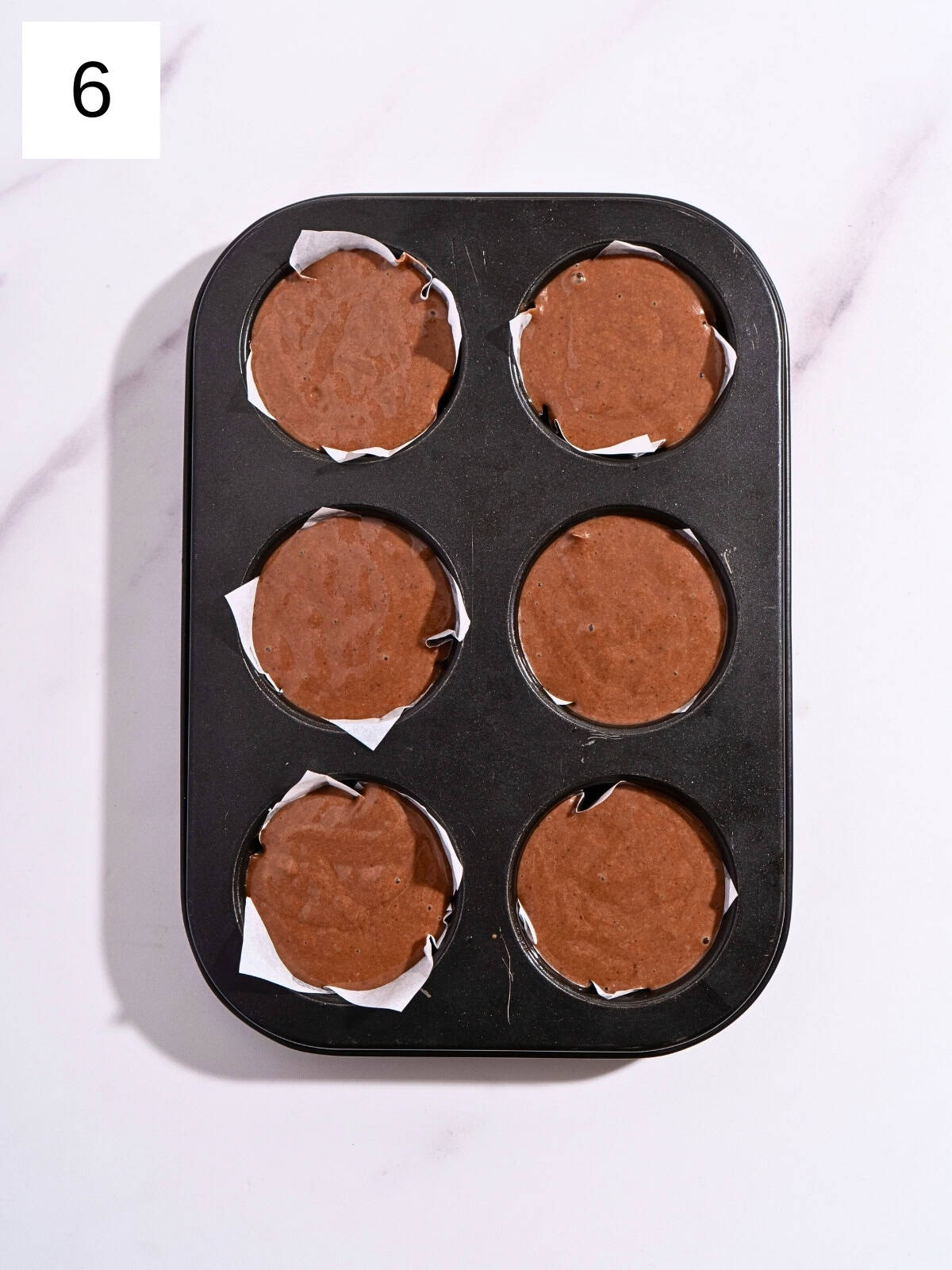 Cupcake liners arranged in a baking tray, filled evenly with chocolate batter.
