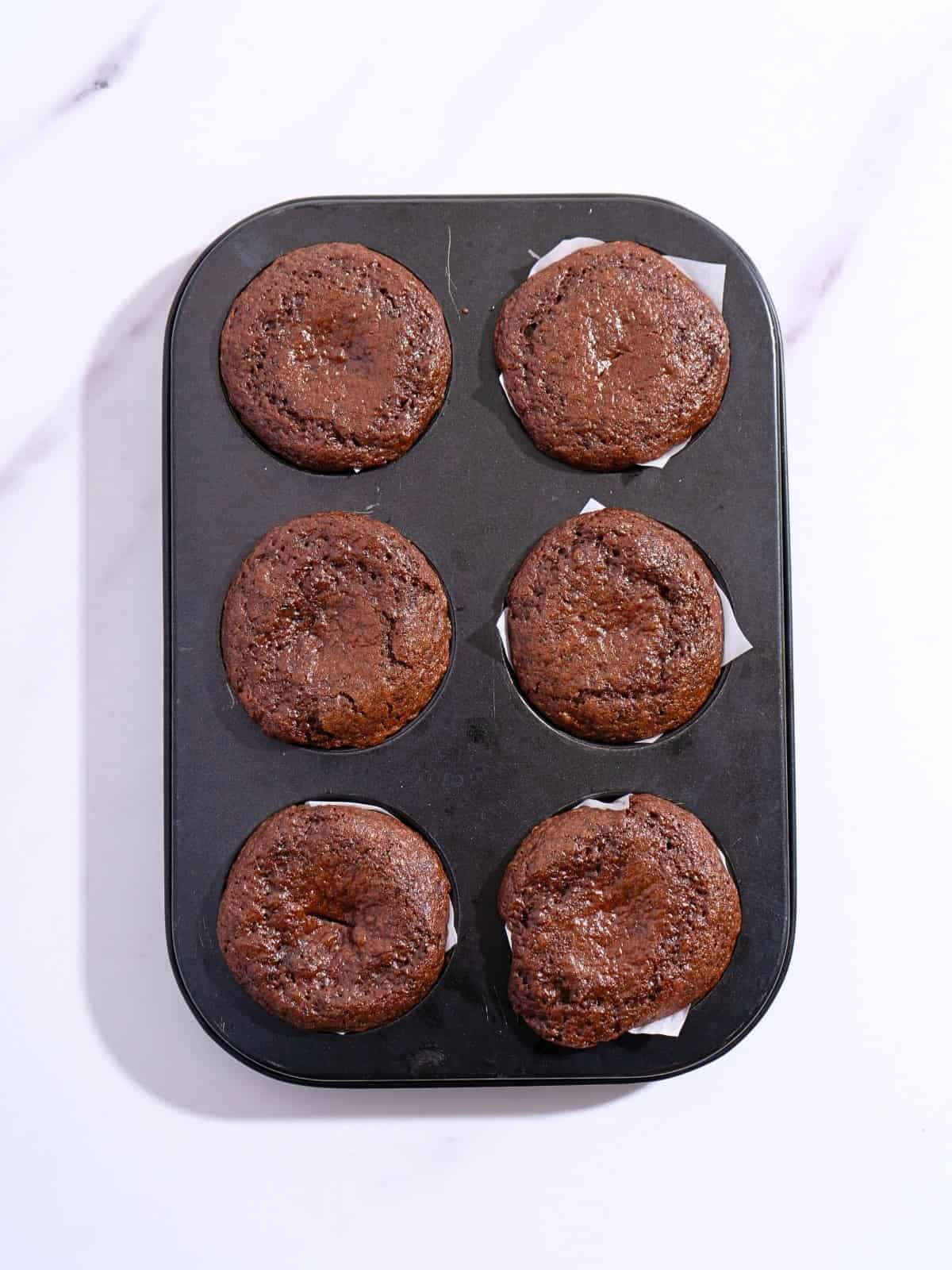 Freshly baked moist chocolate cupcakes cooling in a cupcake baking tray, with a rich, tender texture visible on top.