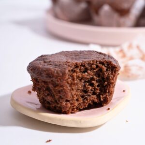 A bitten chocolate cupcake on a plate, revealing its moist and rich chocolate interior.