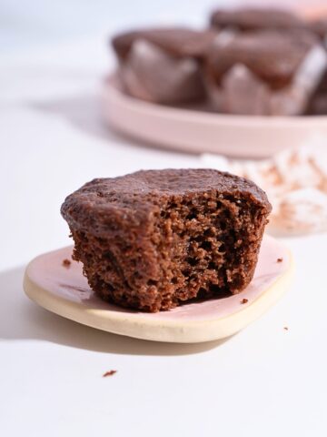 A bitten chocolate cupcake on a plate, revealing its moist and rich chocolate interior.